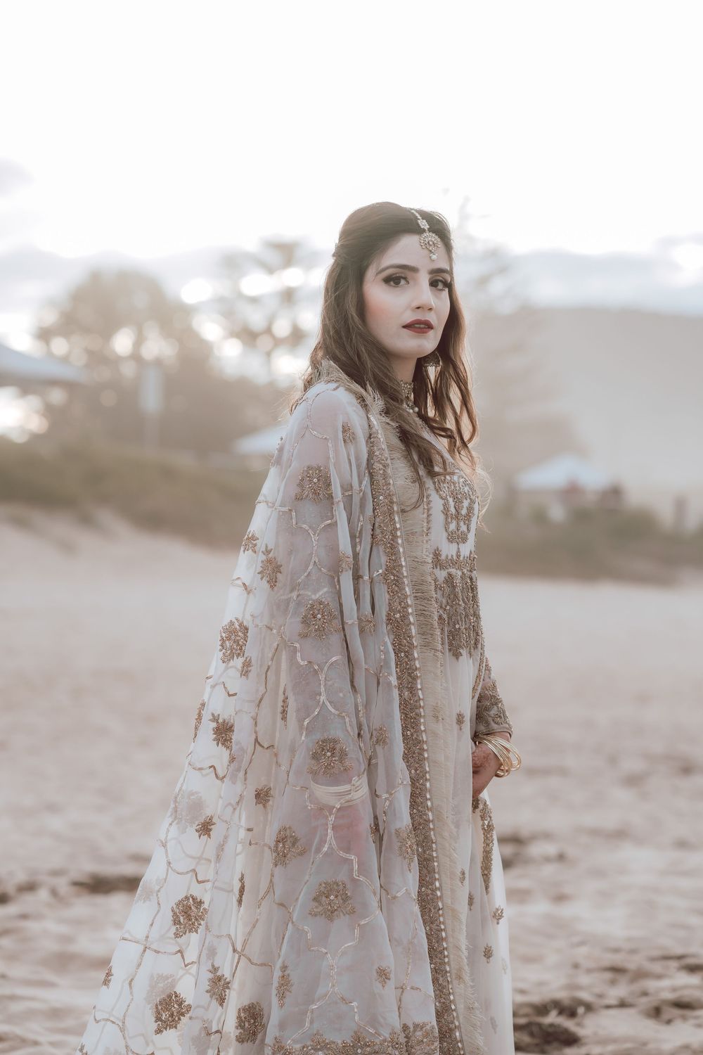 Artistic coastal portrait showing a person wearing an ornate traditional dress with intricate embroidery on sandy shores.