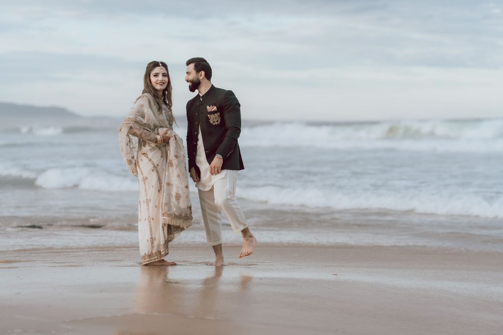 A couple walks along a misty beach shore together during a romantic overcast day.