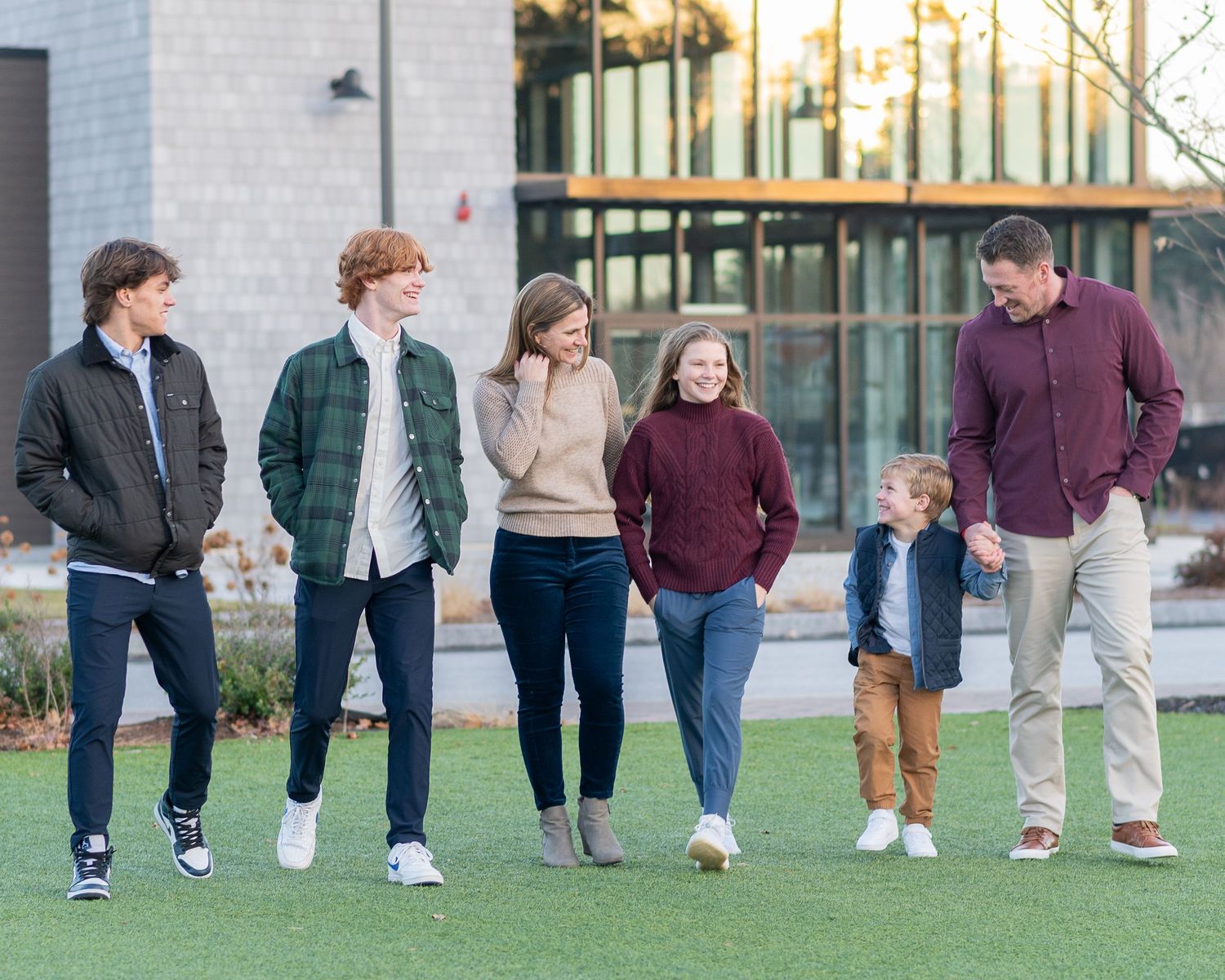 Family members dressed casually in coordinated outfits stand together outside a modern building for holiday photos.