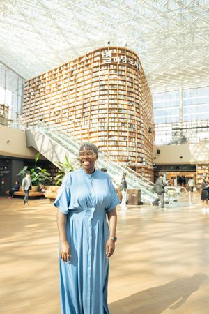 A person in blue clothing poses in front of a curved wall of books in a modern library space.