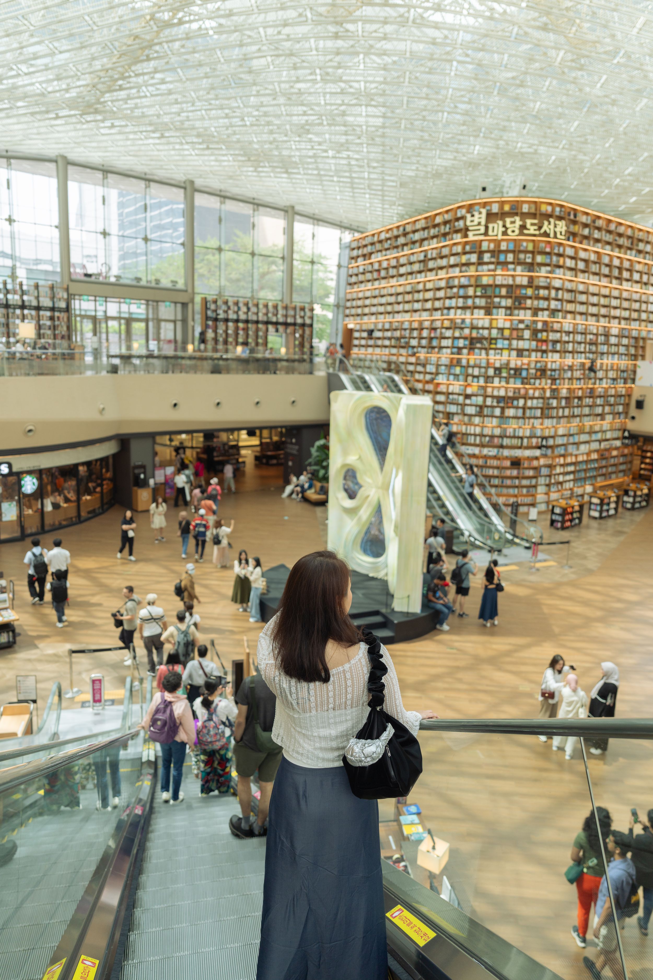 Interior view of a modern library with curved bookshelves and people browsing on multiple levels.