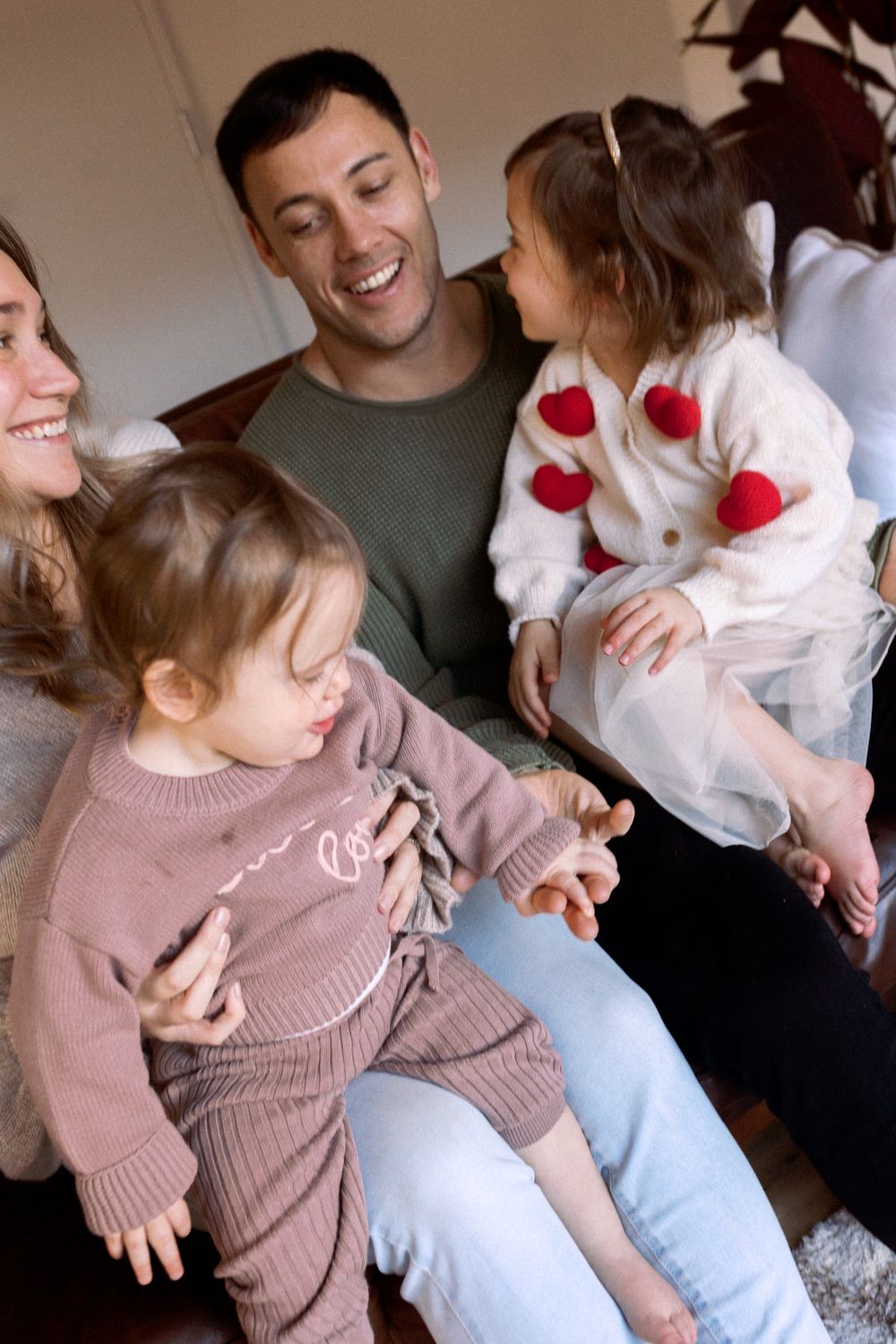 Family members share playful moments on the floor together, wearing matching pink sweaters.