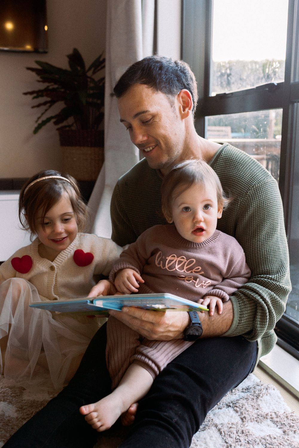 Family relaxing together by a window with natural light streaming in.
