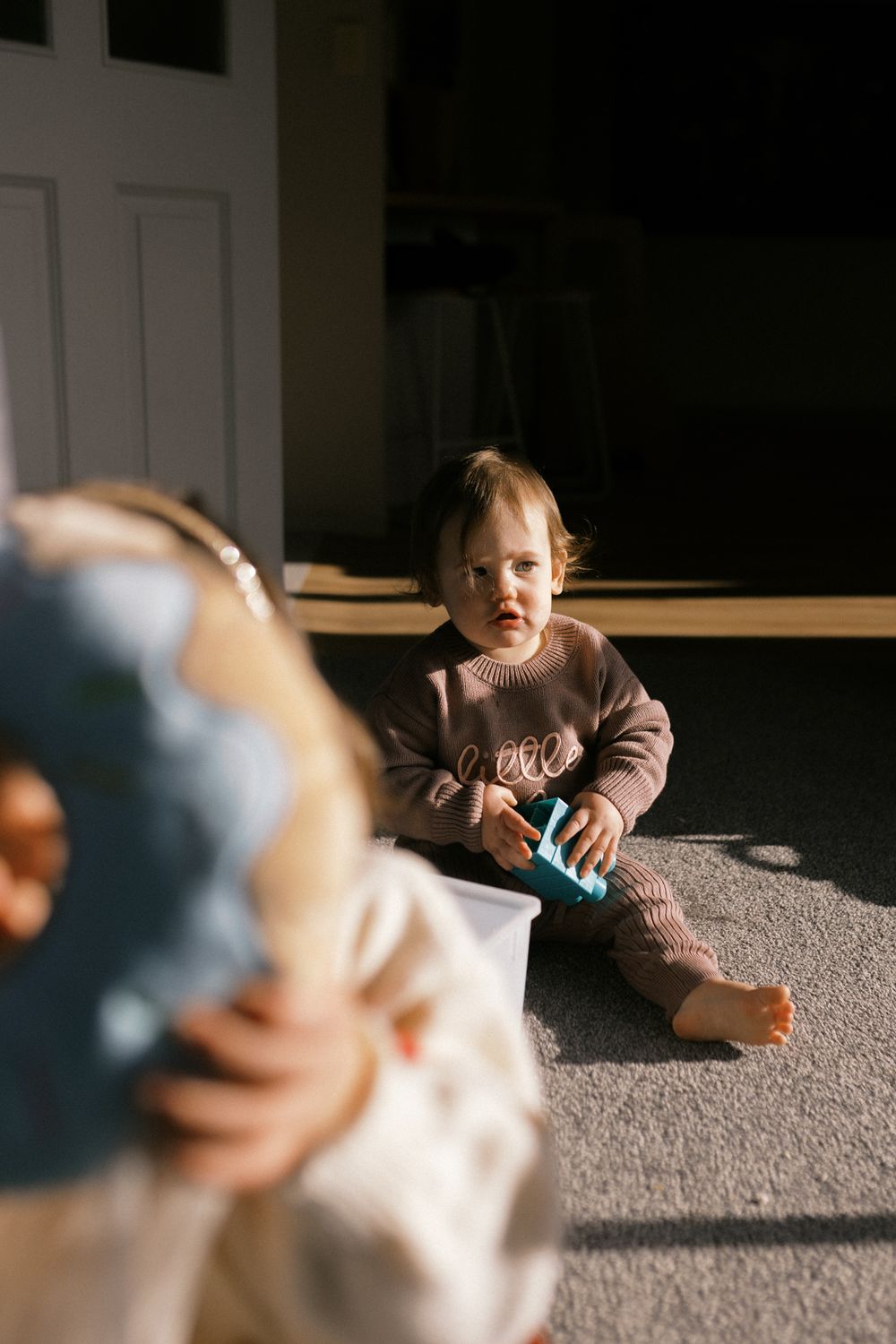 A small figure crawling on gray carpet in soft natural light.