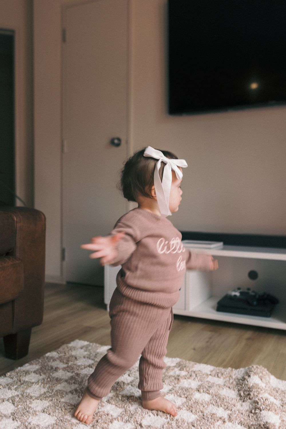 A toddler in a cozy brown knit outfit takes their first steps on a carpeted floor.