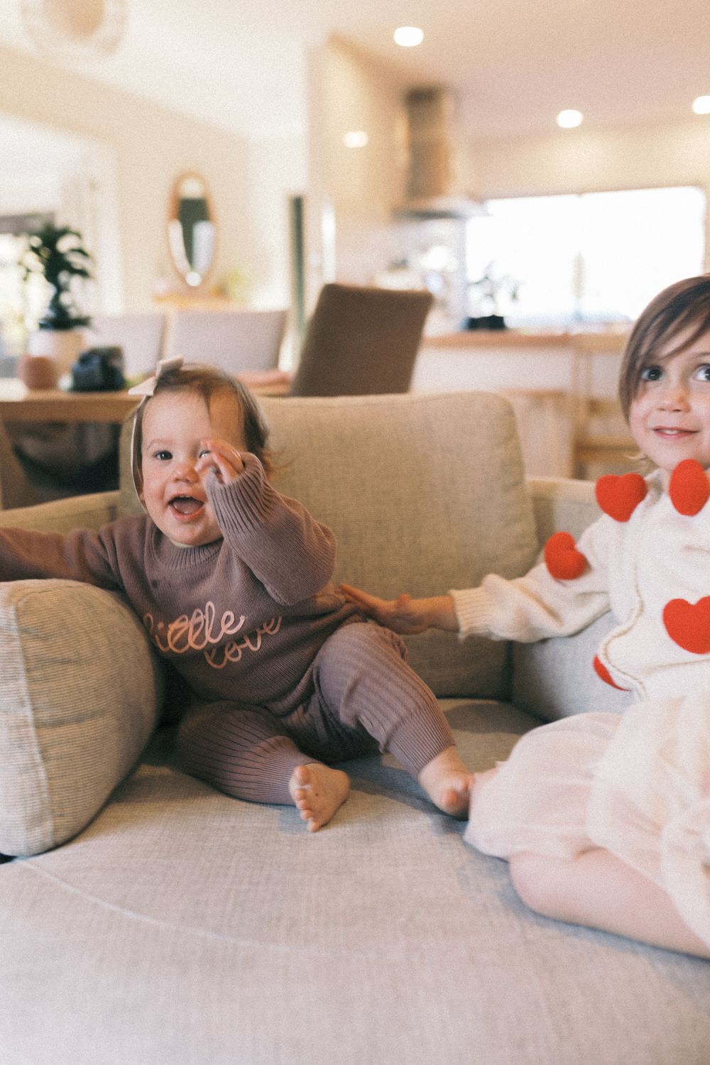 Two people playing and laughing together on a beige couch with heart decorations.