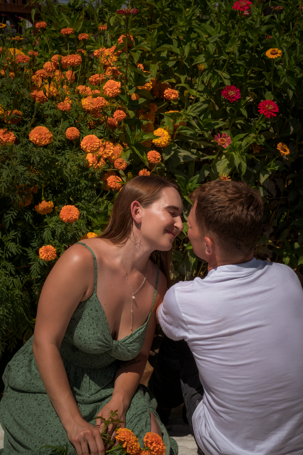 Two people share a playful moment among orange zinnias in a summer garden.