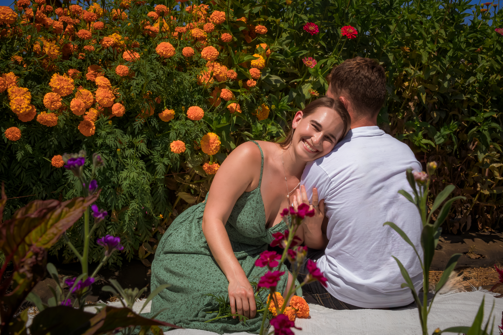 A tender moment captured between two people among orange and purple flowers in a garden.