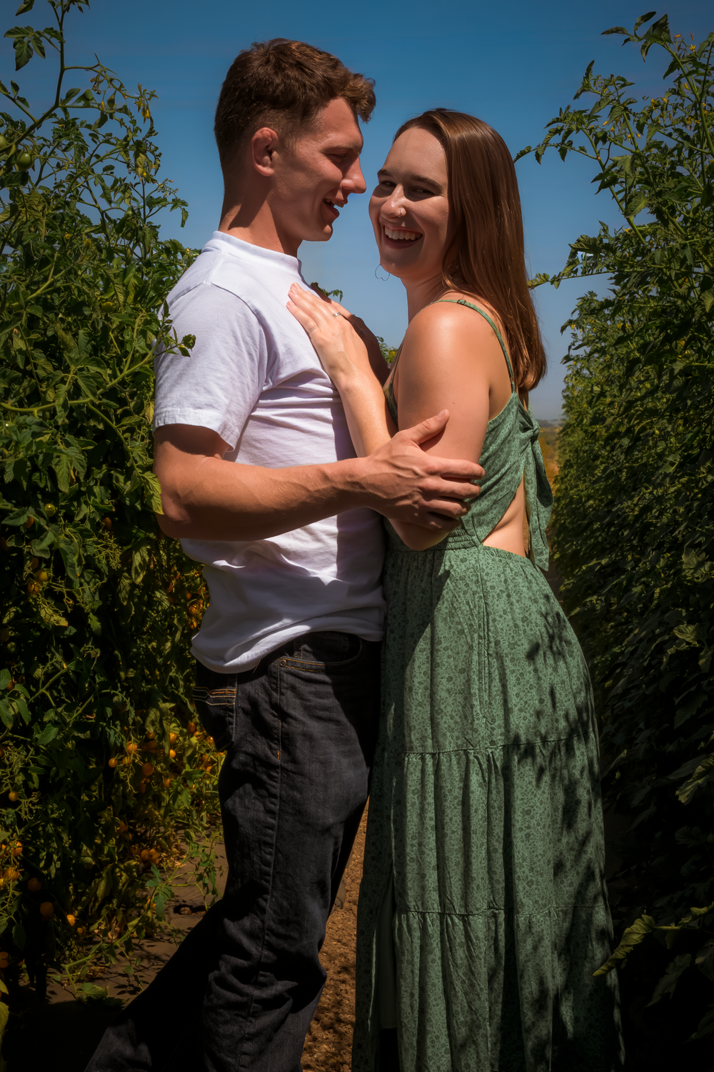 A sweet interaction between two people in a garden with blue sky and green foliage.