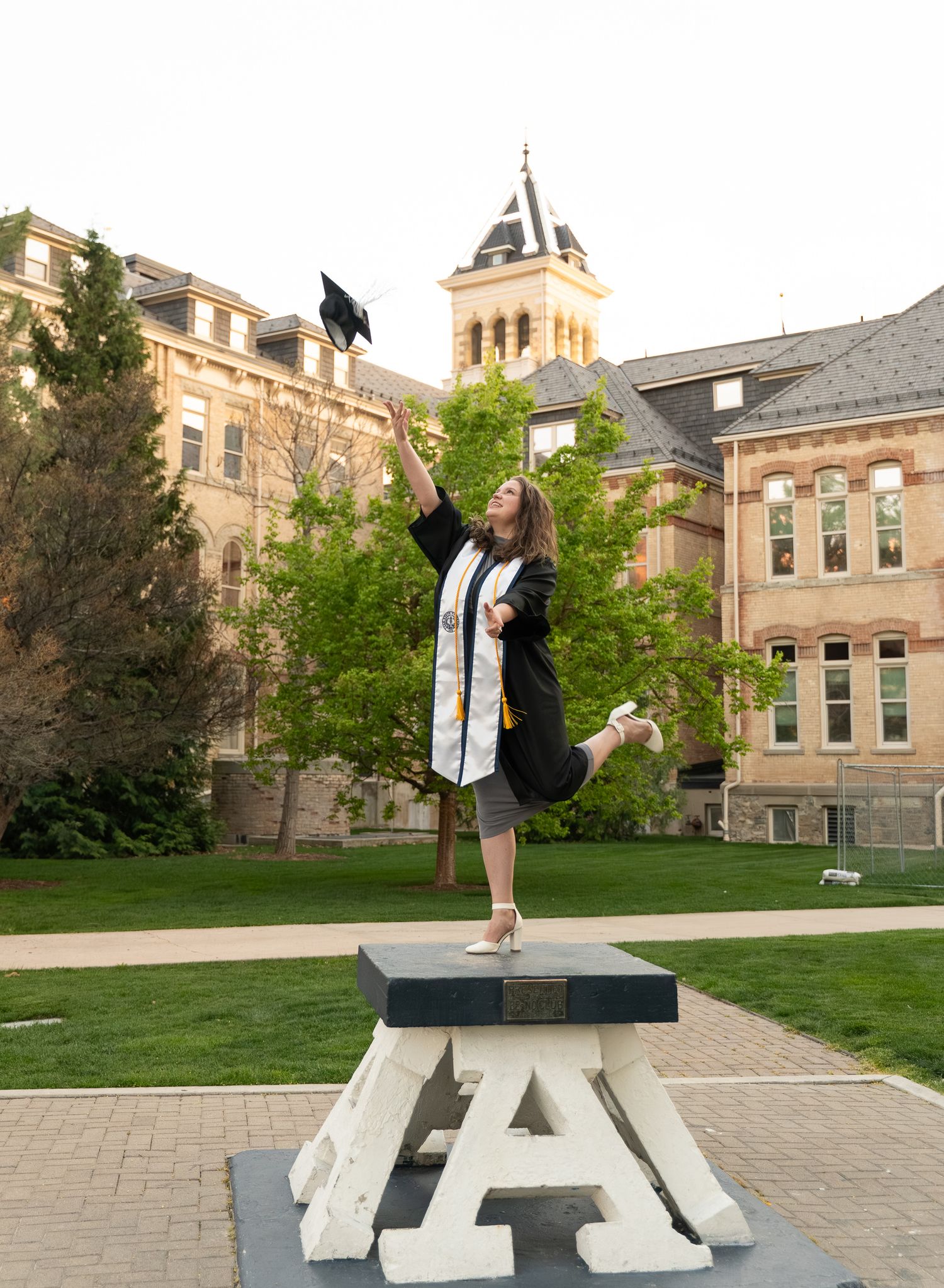 Utah State Grad throwing cap in the air with USU building in the background. Graduation session in Logan UT at USU Campus.