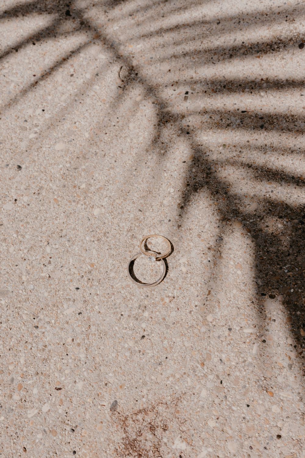 Wedding rings cast shadows on a textured beige surface.