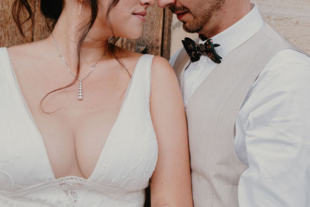 A couple in white wedding attire embracing in soft lighting.