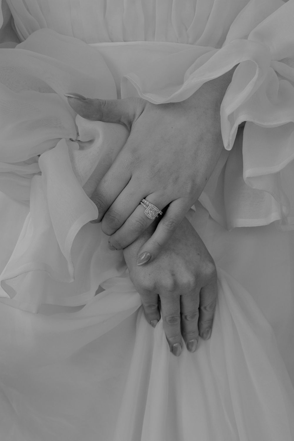 Close-up of hands with wedding rings resting on white fabric.
