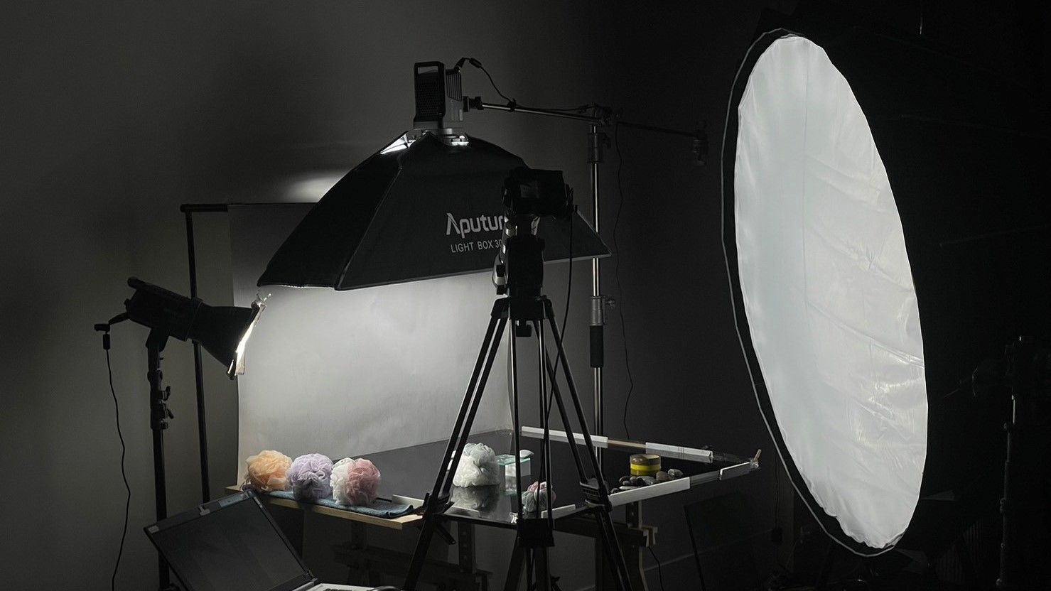 Behind the scenes photo shoot setup showing lighting equipment, reflectors and camera gear in a dark studio setting.