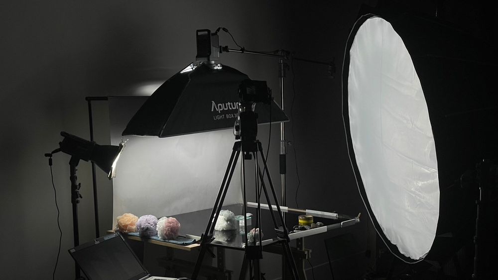 Behind the scenes photo shoot setup showing lighting equipment, reflectors and camera gear in a dark studio setting.