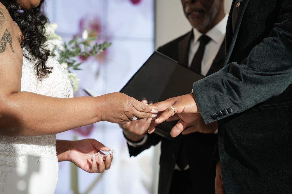 A couple exchanges wedding rings during a romantic outdoor ceremony while guests look on.
