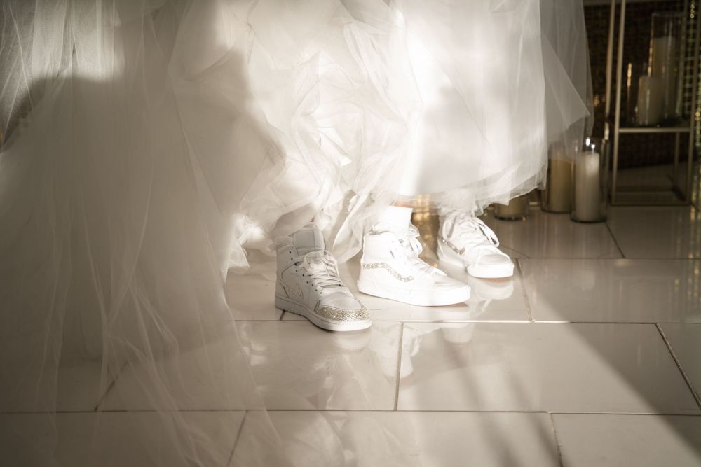 White wedding dress and casual sneakers on a tiled floor illuminated by natural light creating a romantic contrast.