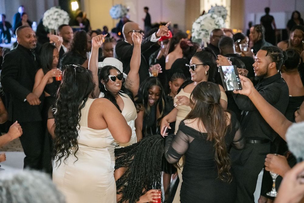 A crowded dance floor at a wedding reception with guests celebrating under decorative lighting.