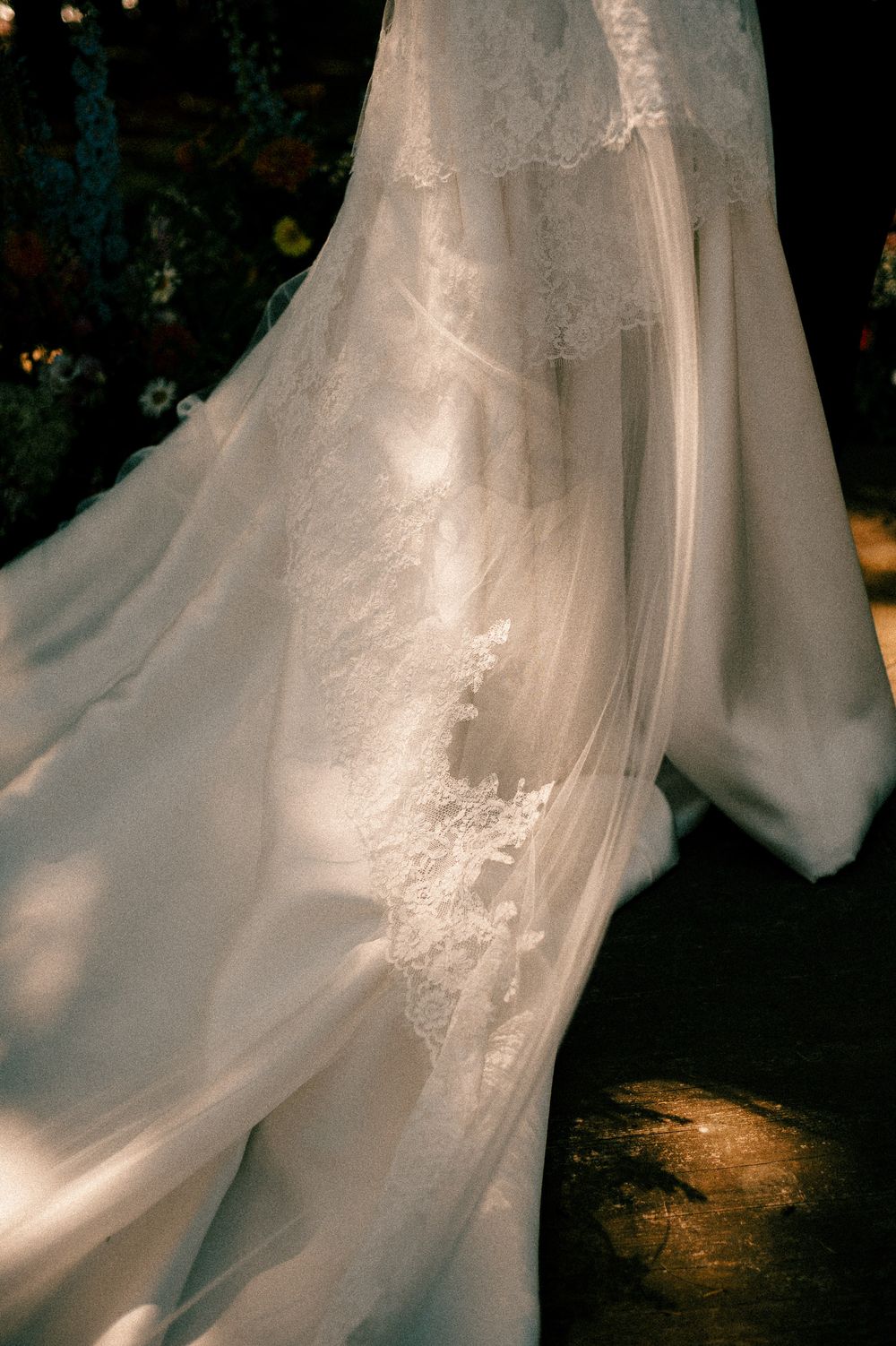 Close-up view of ethereal white gown with delicate lace details and flowing fabric in a dark setting.