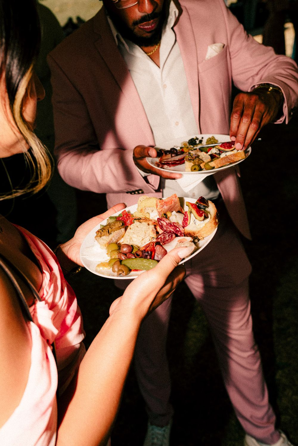 People at a party passing plates of gourmet appetizers and snacks at a dim evening event.