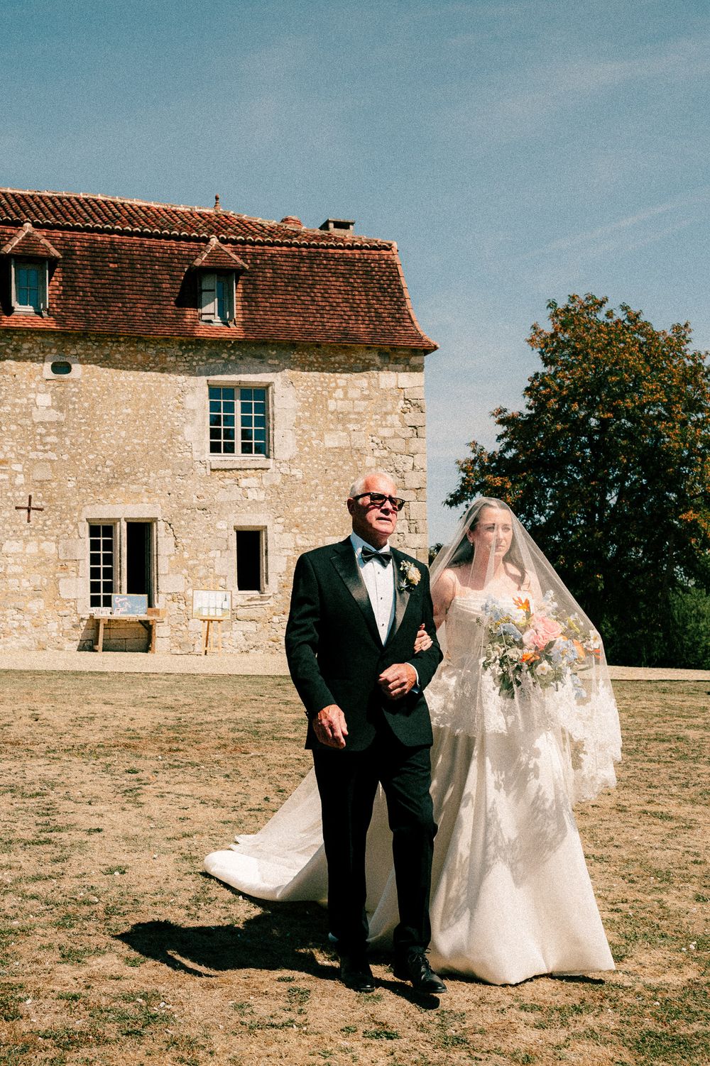 A wedding photo series outside a rustic stone farmhouse with sunlit countryside backdrop and architectural details.