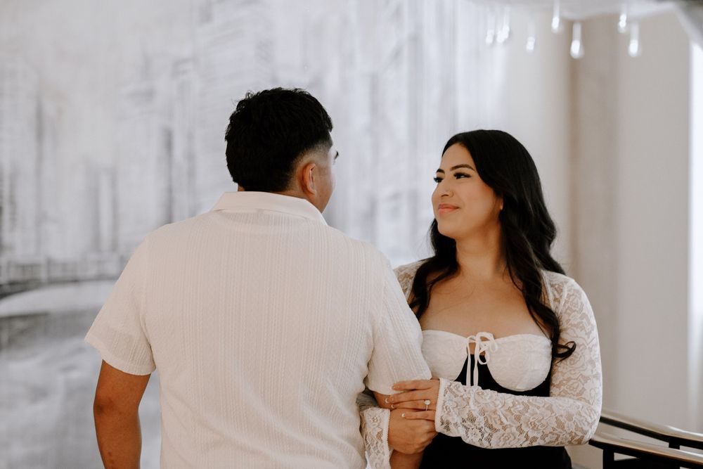 A couple shares a joyful moment together in a white room, with one person wearing a white shirt and another in a lace top.