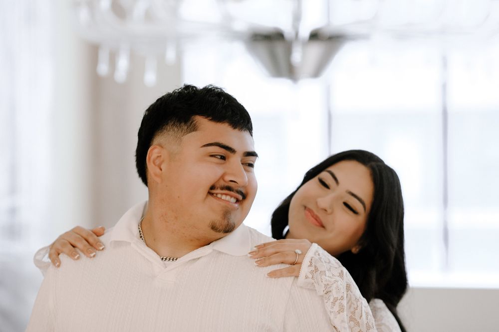 A couple shares tender moments of affection and laughter in an intimate indoor photoshoot with natural lighting.