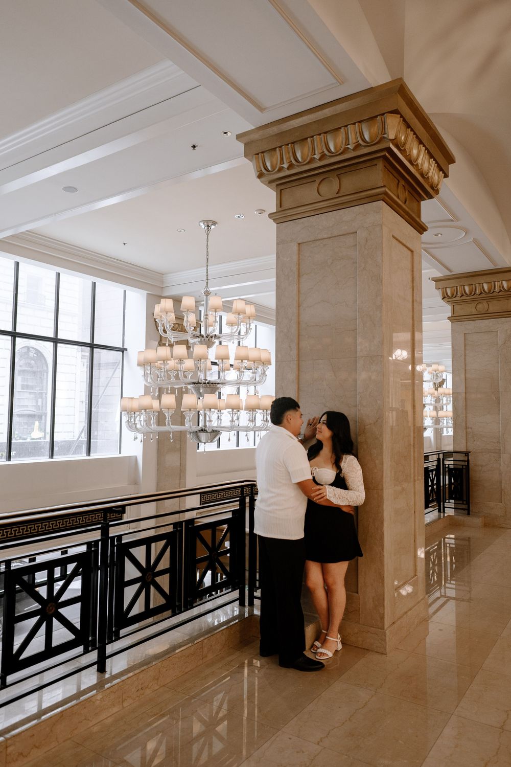 An elegant building interior with decorative columns and lighting fixtures features two people in a romantic moment.