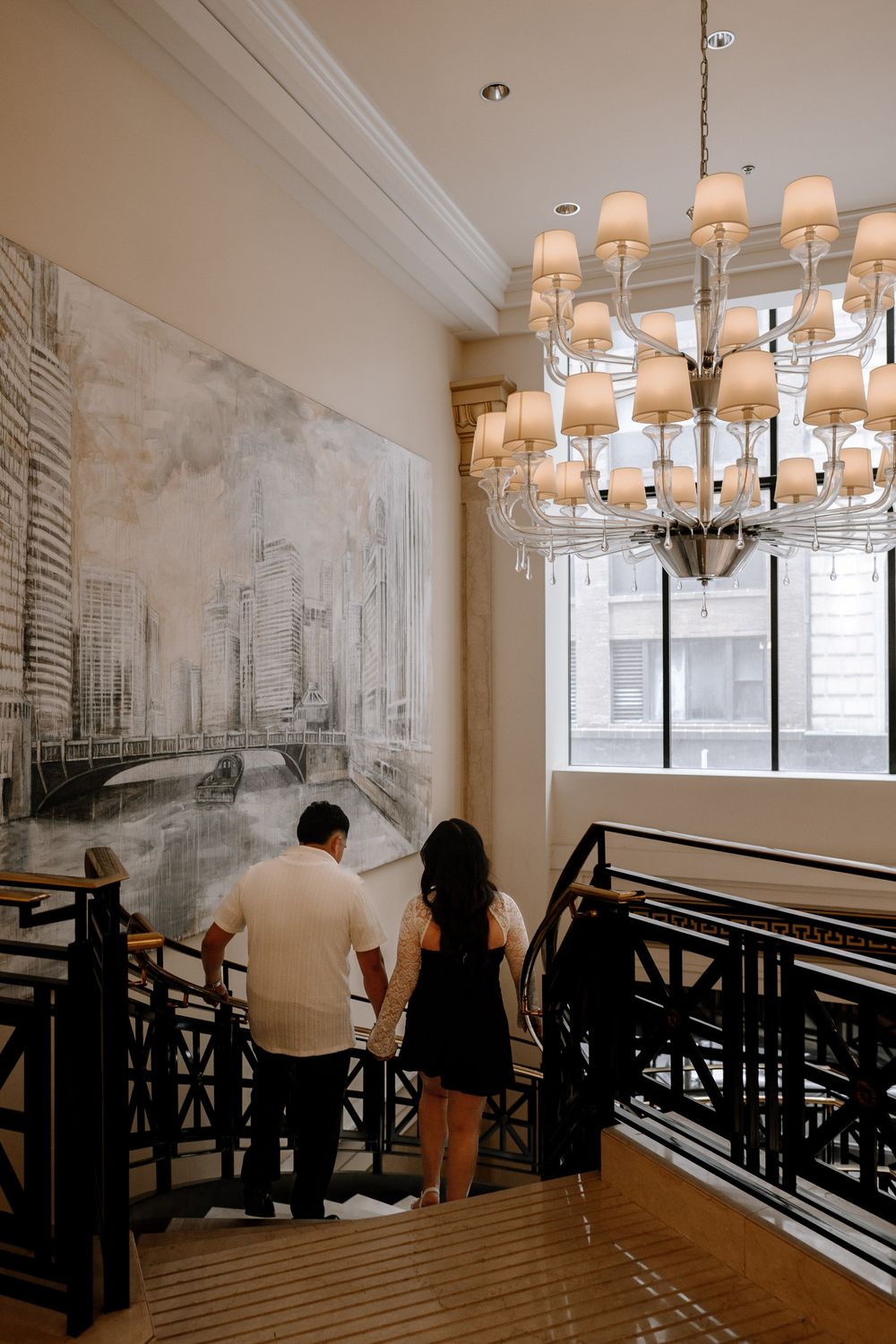 Interior seating area with black railings and white walls featuring vintage city murals and elegant chandelier lighting.