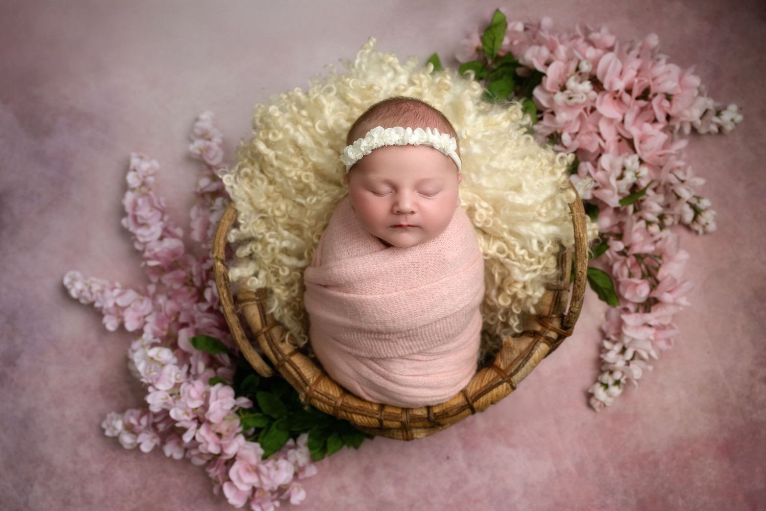Professional newborn photography composite showing sleeping baby posed with soft pink cherry blossoms in studio lighting.