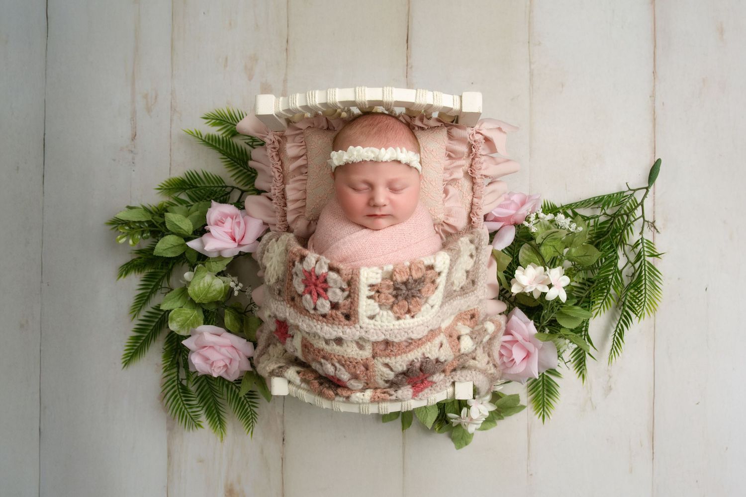 Five connected portrait style photos of a sleeping baby ornately posed with flowers and pink decorative elements on a white wooden backdrop.