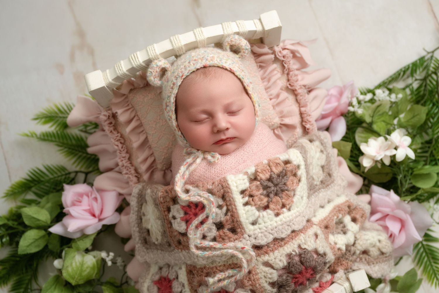 Sleeping newborn baby nestled in pink floral decor with delicate lace and greenery accents.