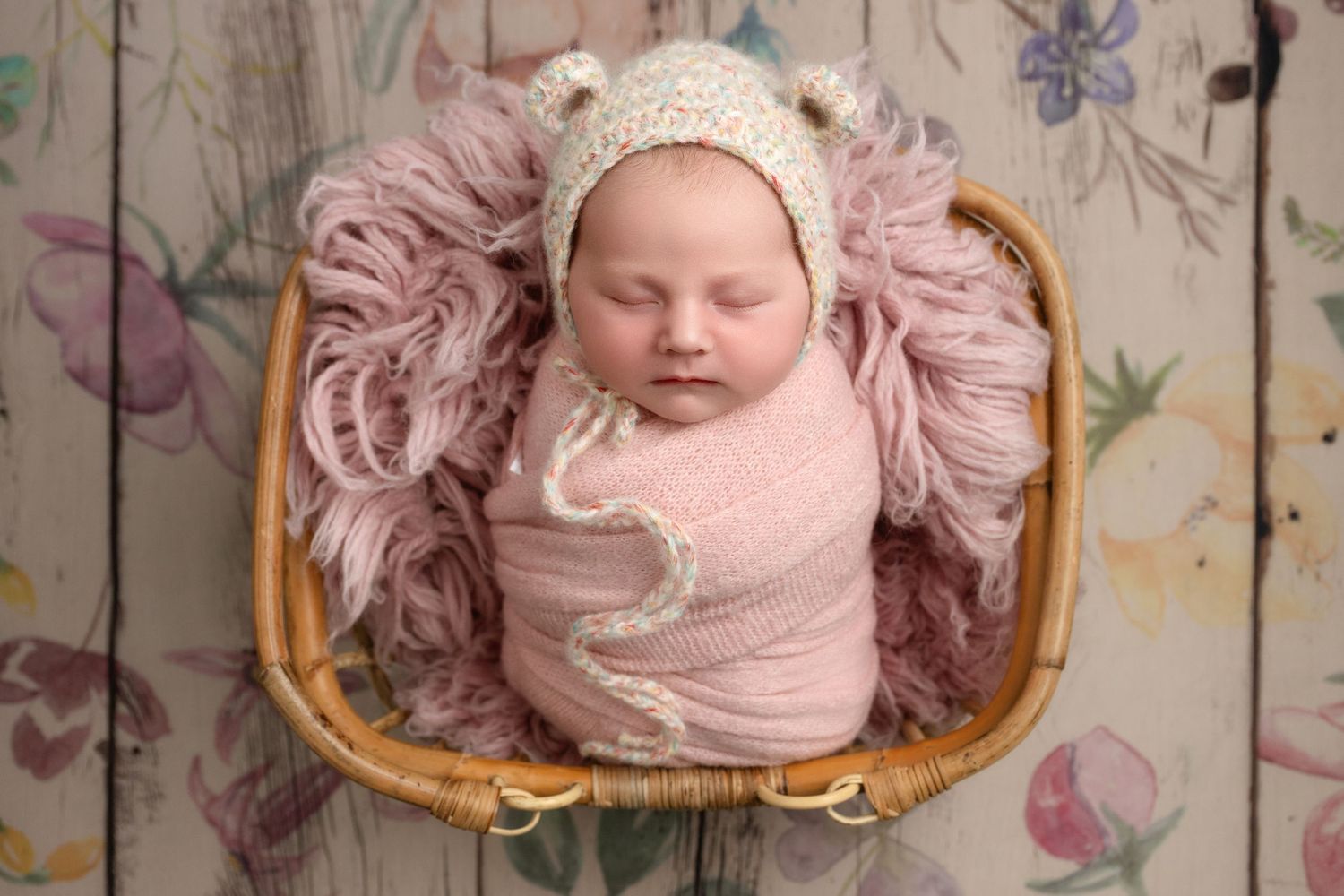 Swaddled newborn lies on vintage frame adorned with delicate pink flowers and decorative elements.