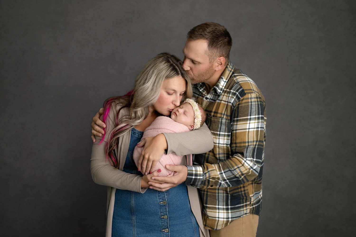Couple in plaid shirt and gray sweater embraces tenderly against dark gray backdrop in photo series.