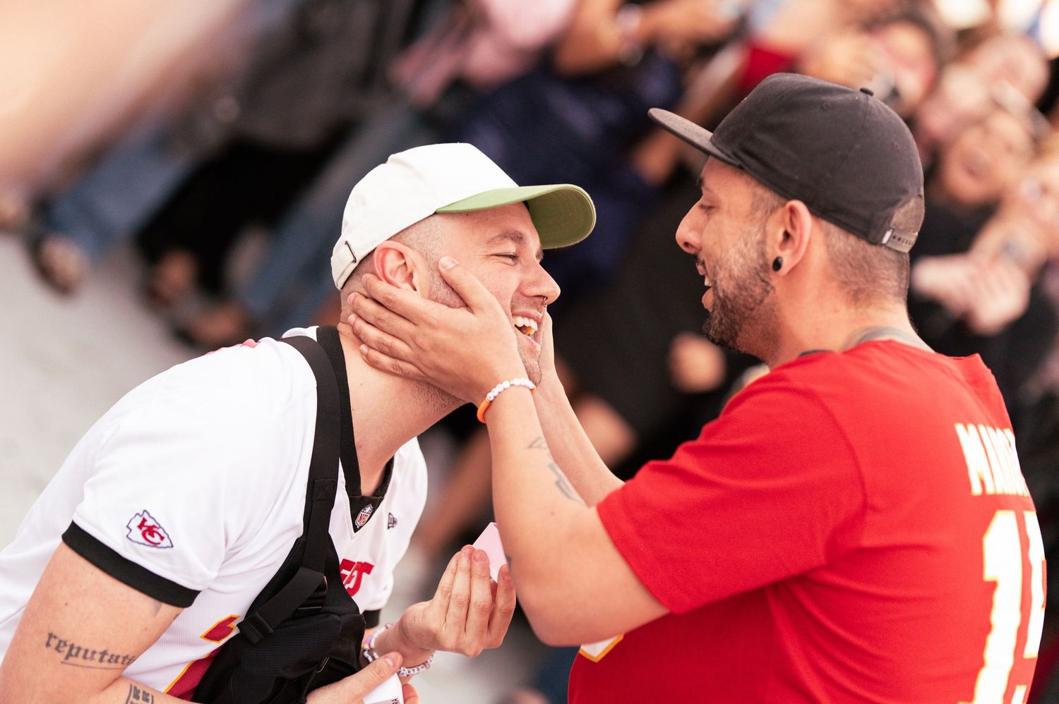 Two sports fans share an emotional moment at a game, one wearing white and one in red.