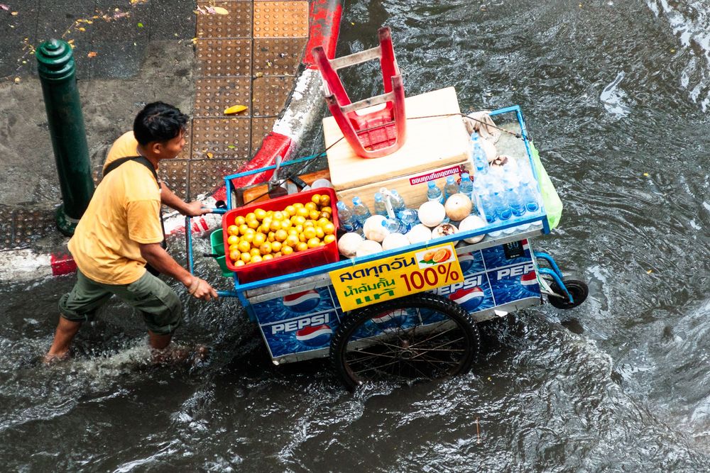Street vendor pushes their cart through deep flood waters during heavy monsoon rains in Bangkok.