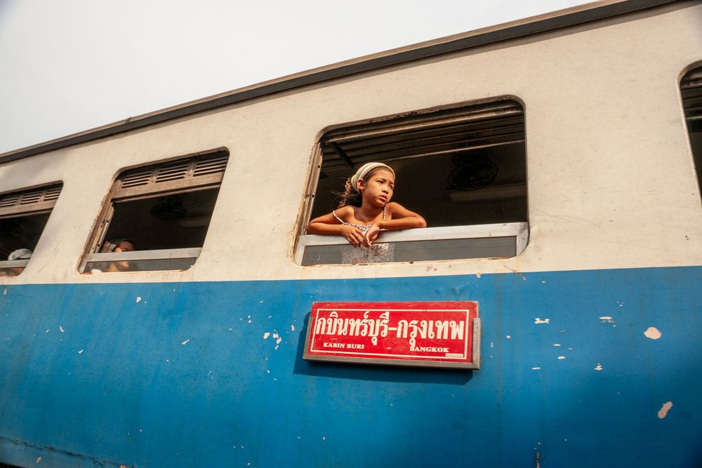 Train passengers peer out of windows in a vintage railway car captured from the exterior perspective.