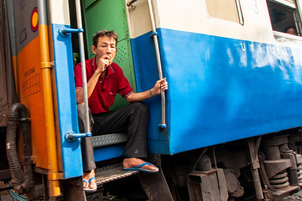 Train passengers board a vibrant blue and orange railway car on a sunny day.