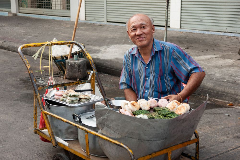 Street vendor preparing Thai food from a traditional wooden cart on an urban sidewalk.