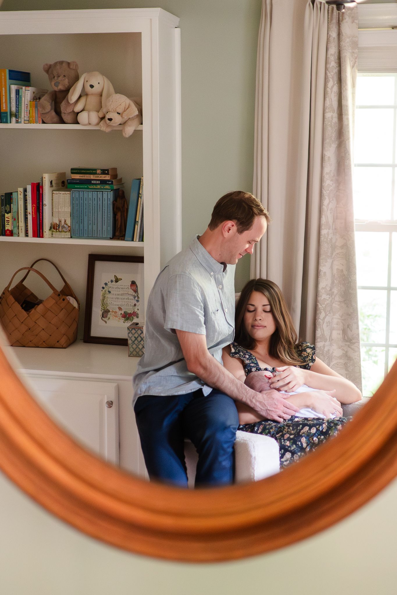 Reflection in curved mirror shows a couple resting together on a couch with white built-in bookshelves in background.