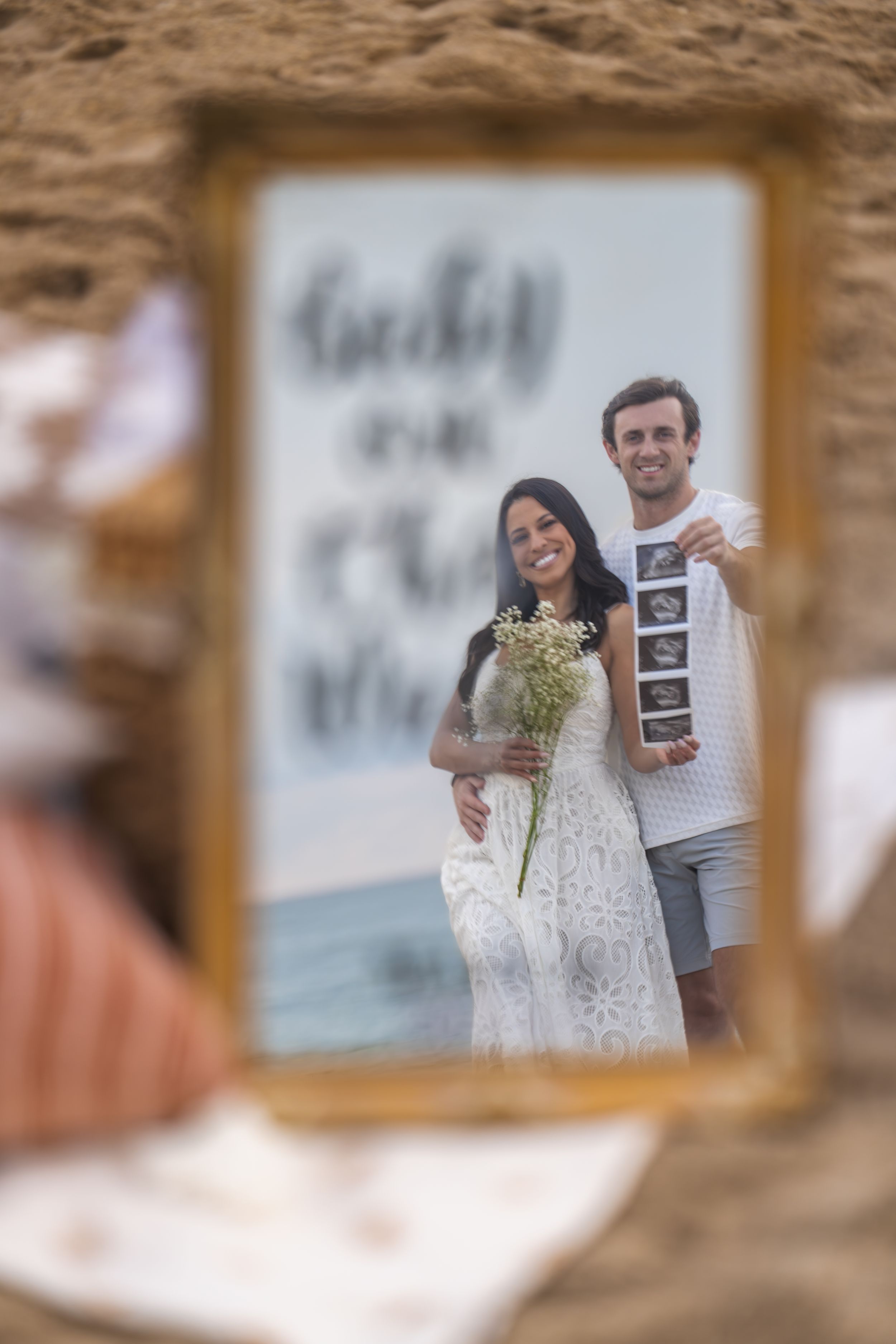 Couple on beach sharing exciting news with ultrasound photos.