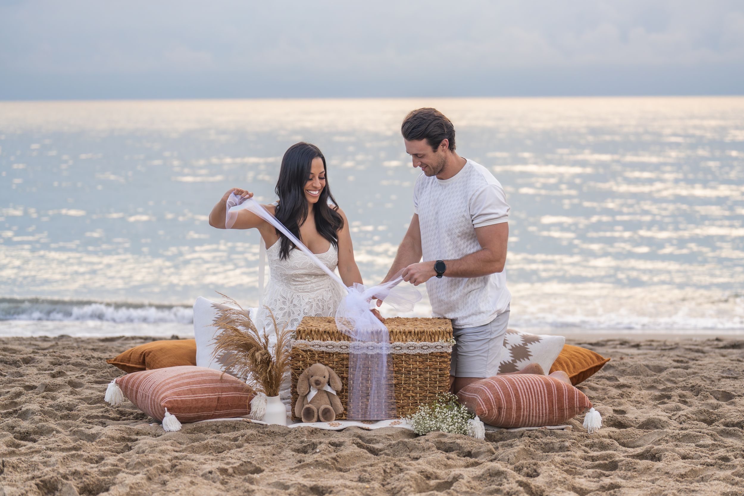 Romantic beach picnic setup with wicker basket and blanket at sunset.