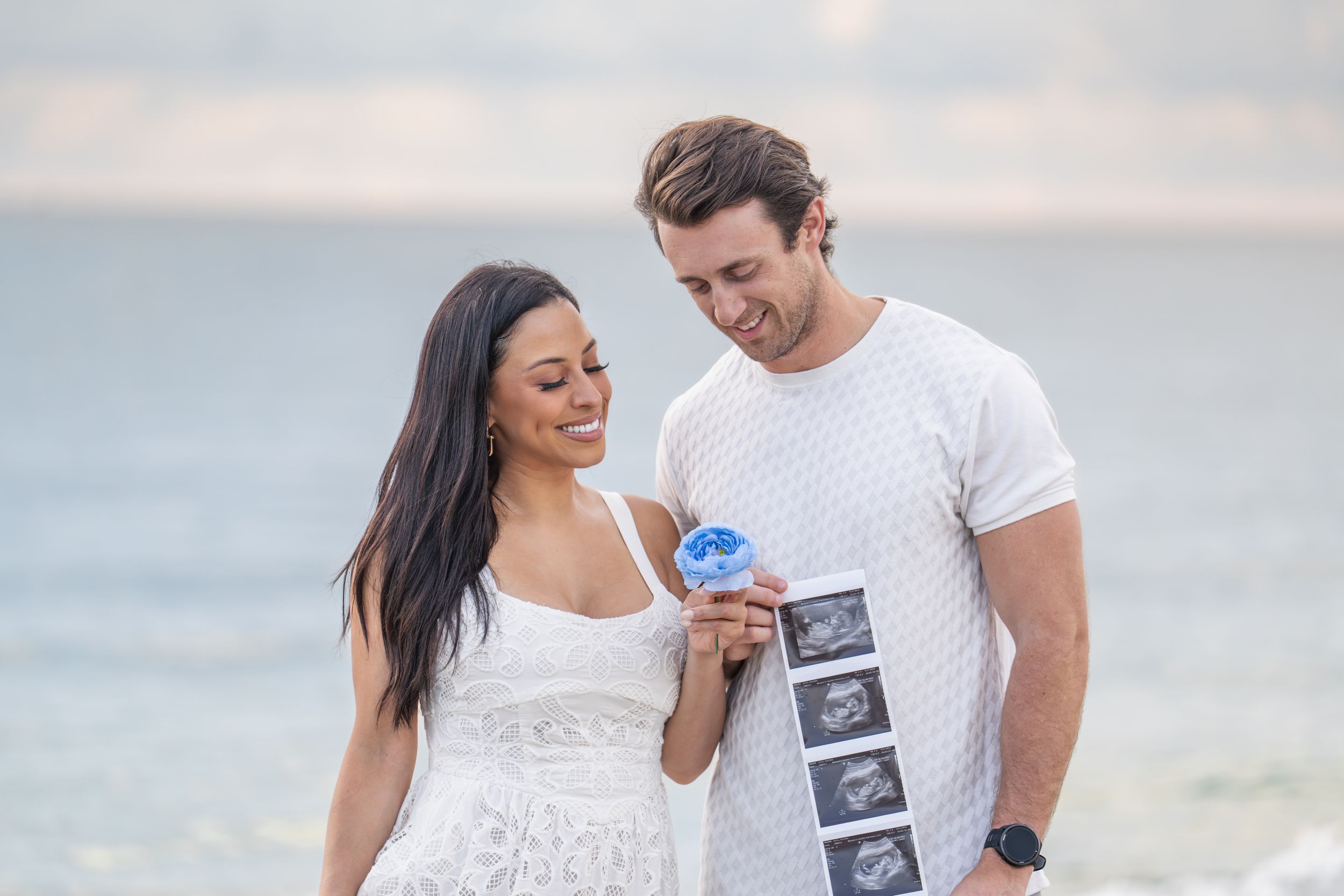 Happy couple sharing pregnancy announcement with ultrasound photos on sunny beach.