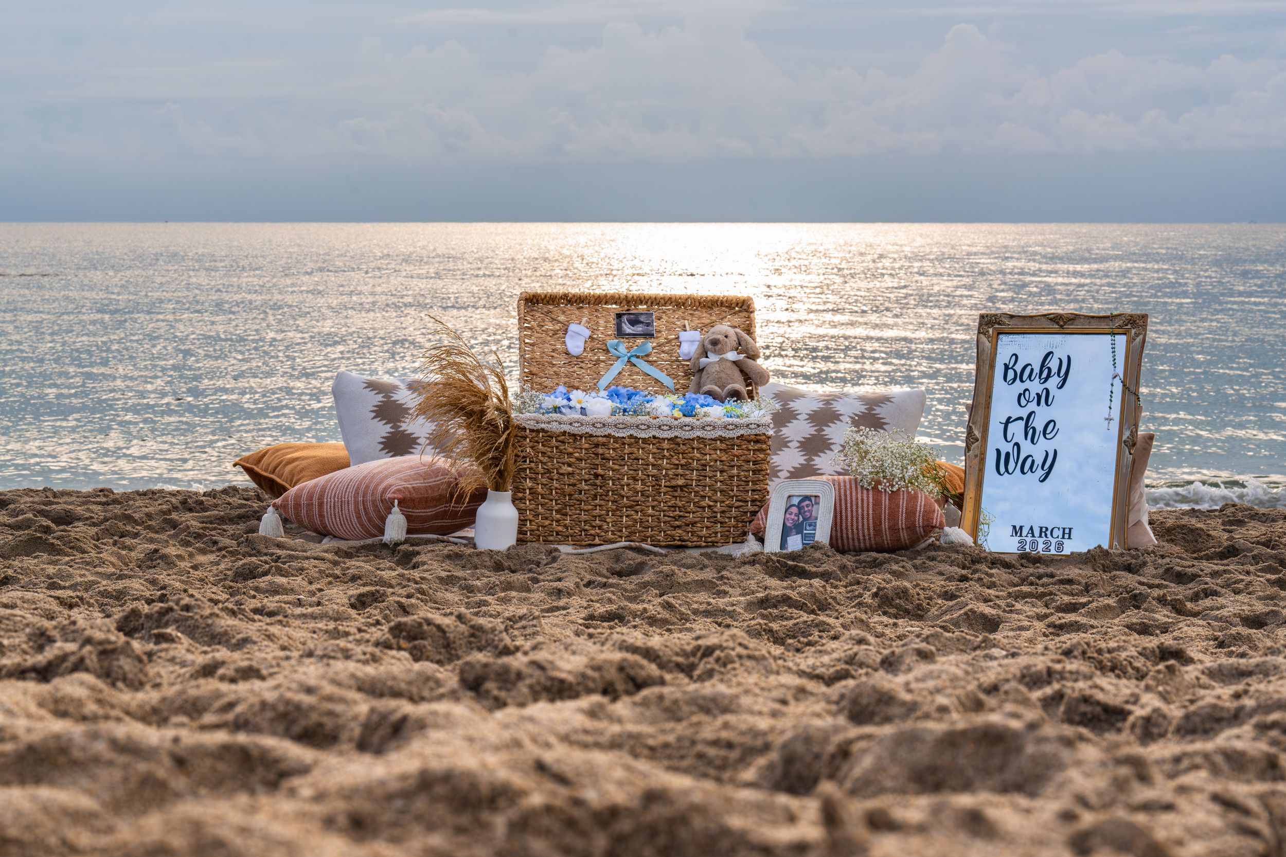Beach pregnancy announcement setup with picnic basket and sonogram photos at sunset.