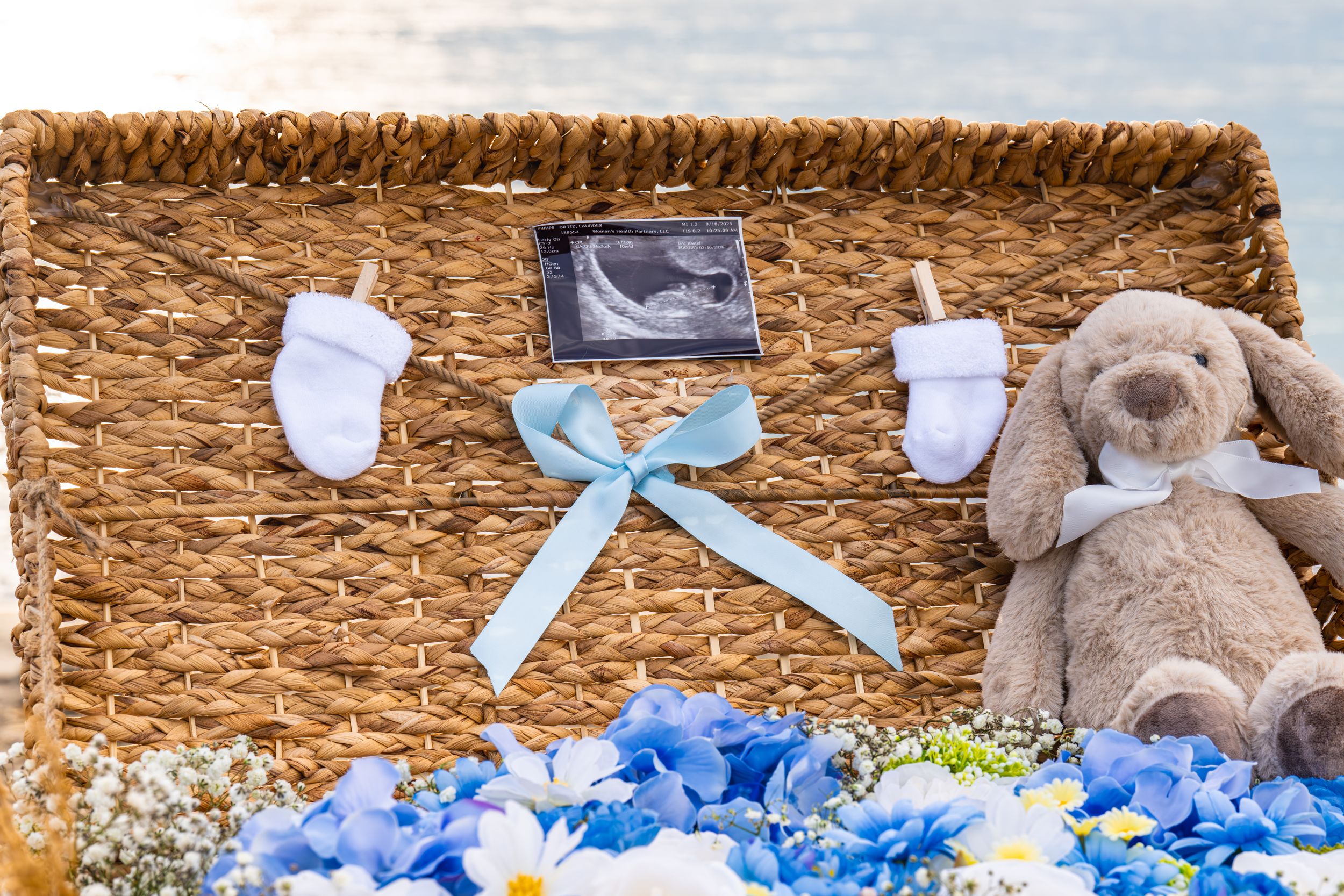 Decorative display with teddy bears, blue ribbons, and floral arrangements on woven background.