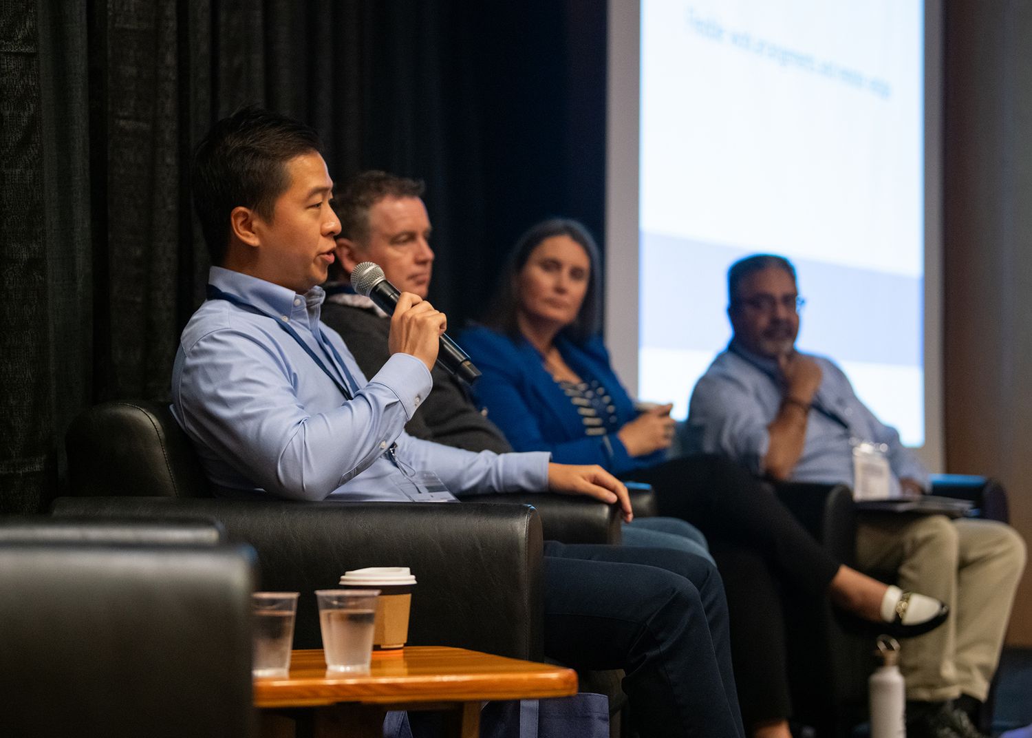 Panel discussion at a conference with four speakers seated on stage, one speaking into a microphone.