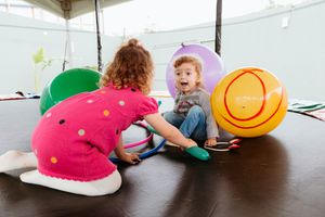 Children engaged in movement activities with large plush toys under a covered outdoor area.