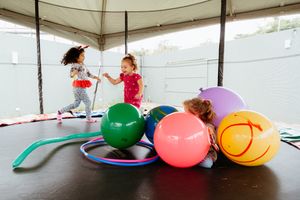 Kids enjoying playtime with oversized soft toys and balloons in a bright covered space.