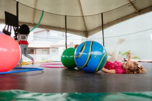 A group of kids take part in an active yoga exercise class doing stretches on colorful mats in a covered space.