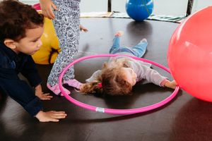 Children crawl under colorful balloon arches during an indoor party activity.